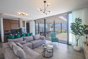 A modern living room with a sofa, coffee table, and a view of the outdoors. - Brand New 4 Bedroom Villa in Protaras Center (Paralimni)