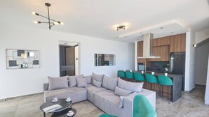 A modern living room with a sectional sofa, a coffee table, and a dining area with bar stools. - Brand New 4 Bedroom Villa in Protaras Center (Paralimni)