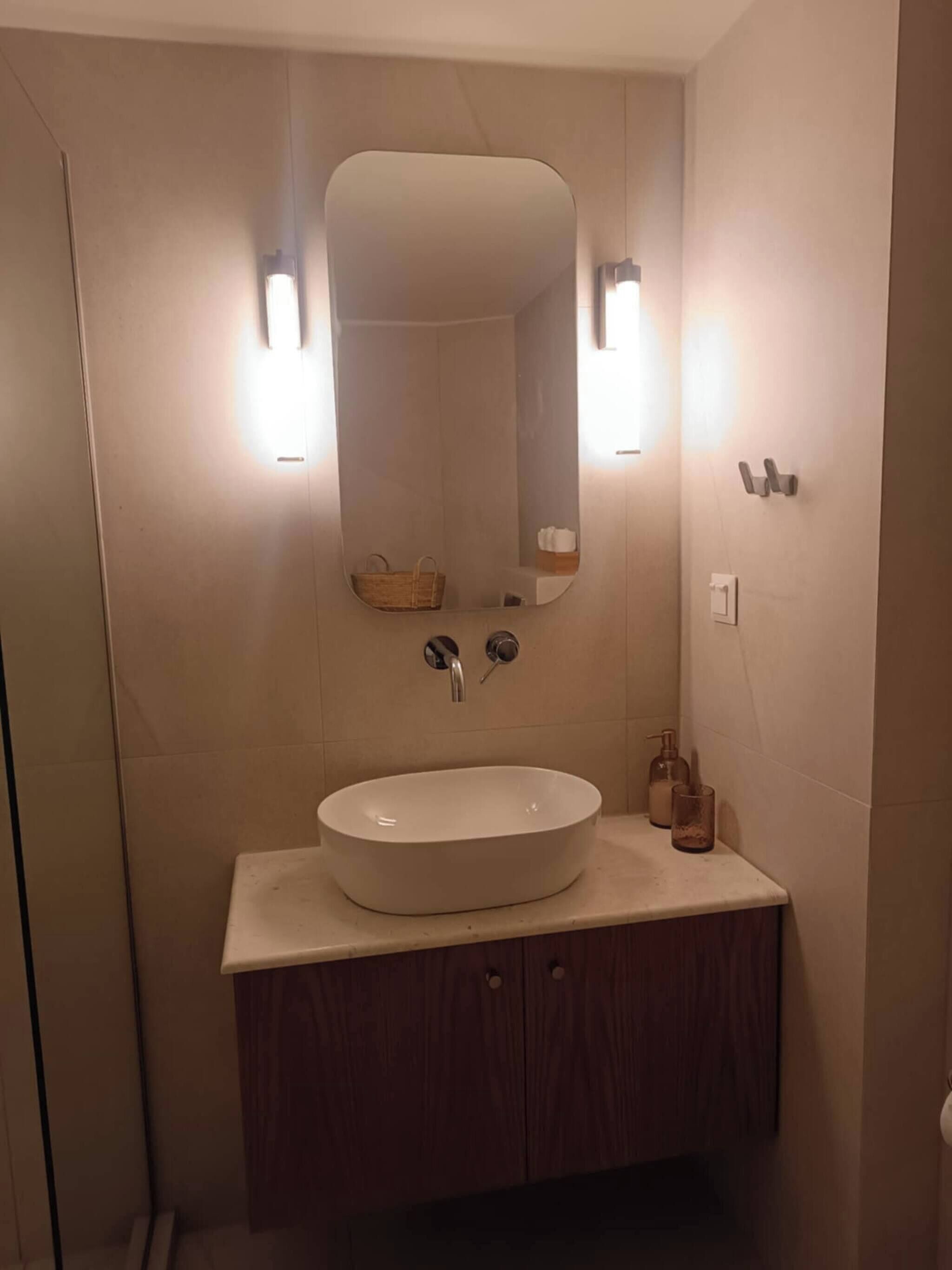 A bathroom with a white sink, wooden vanity, a mirror, and two wall-mounted lights.