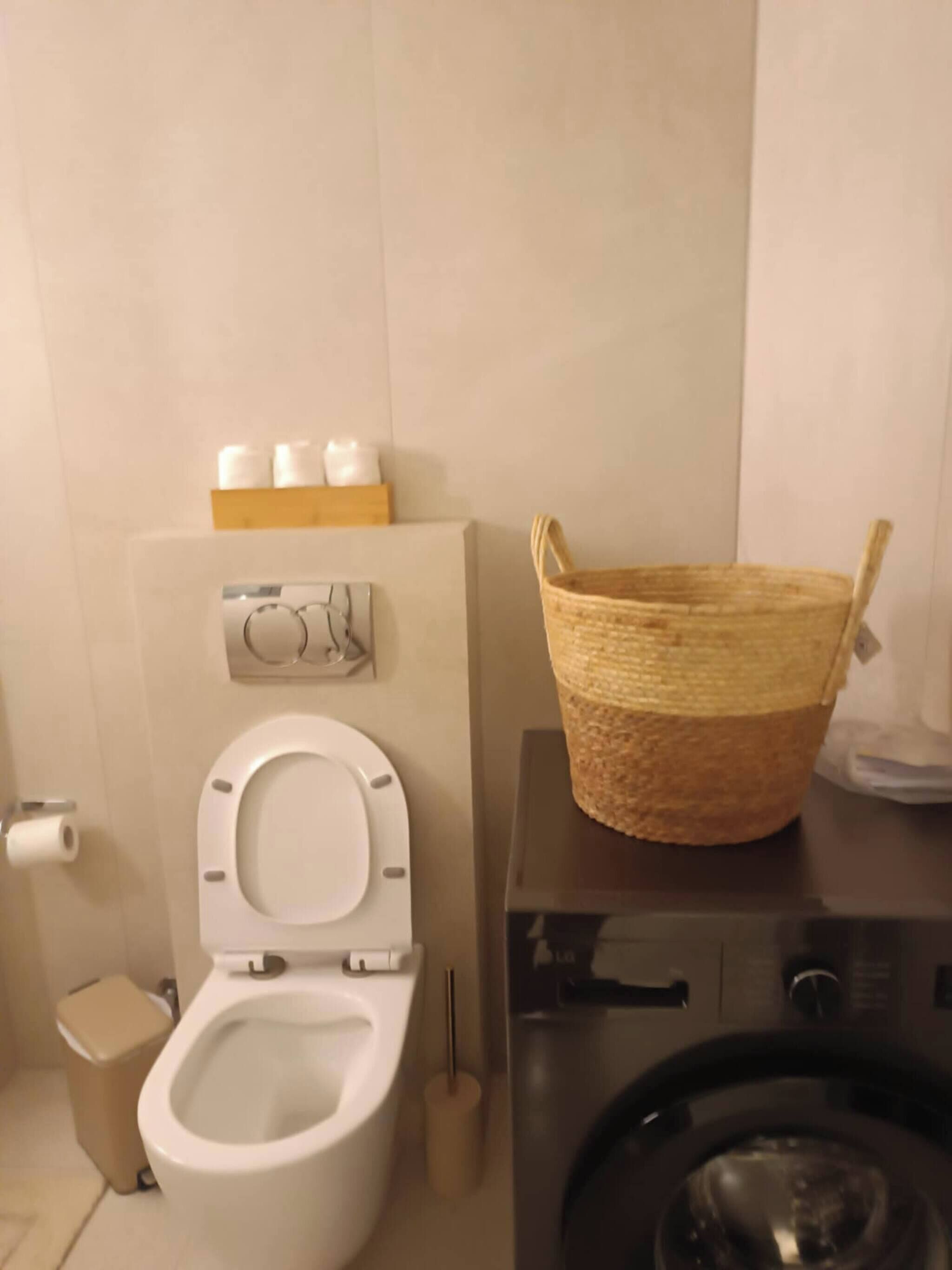 Un baño con inodoro, lavadora y una cesta encima de la lavadora.