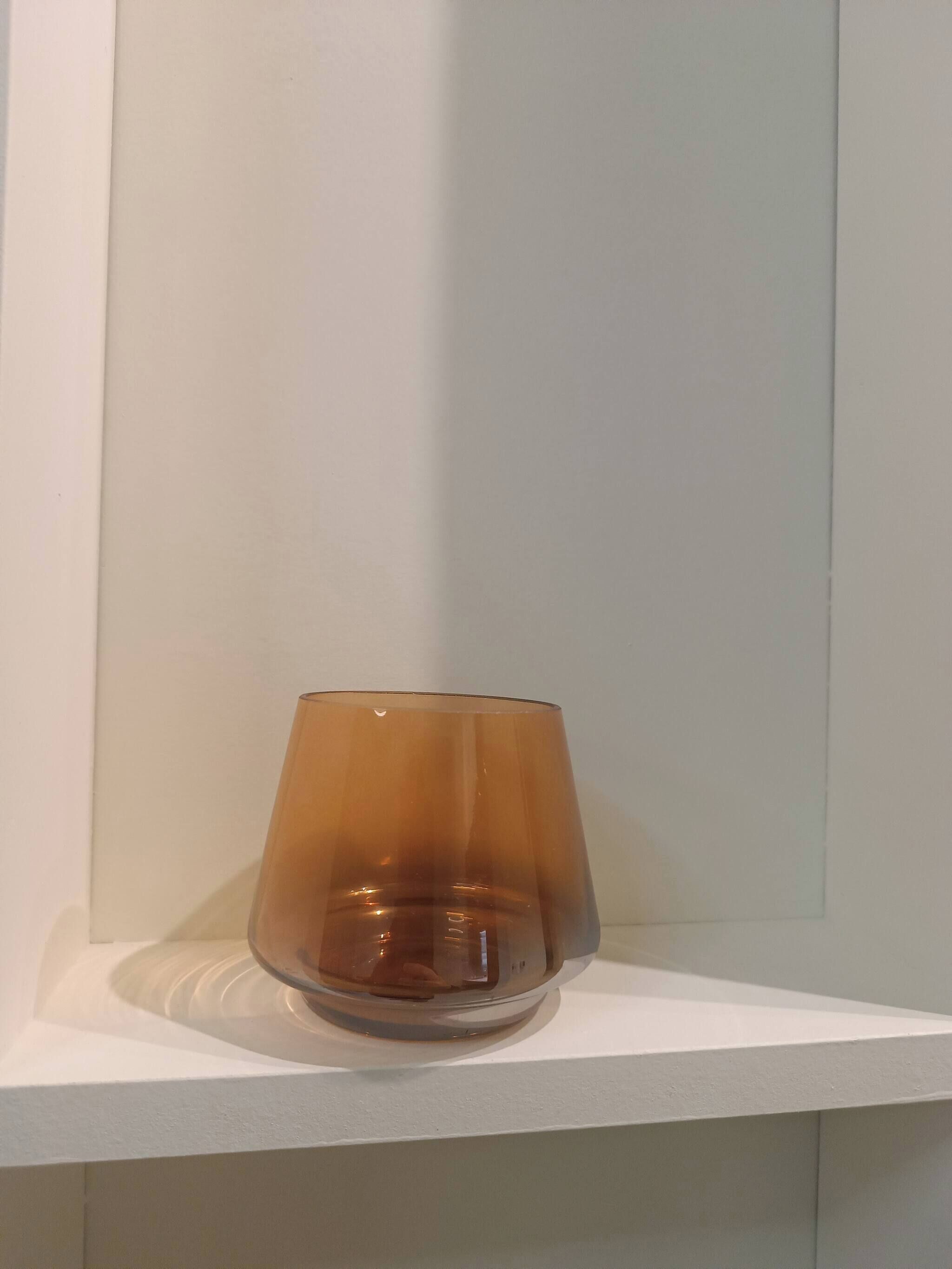A clear glass on a white shelf against a white wall.