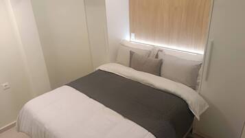 Un dormitorio con cama, almohadas, cabecera con iluminación integrada y armario.