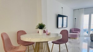Un comedor moderno con una mesa de mármol, cuatro sillas rosadas, un taburete con patas doradas y una planta en maceta.