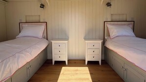 A bedroom with two single beds, a nightstand with drawers, and a wooden floor.