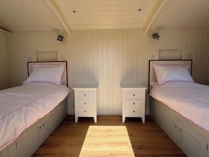 Un dormitorio con dos camas individuales, una mesita de noche con cajones y suelo de madera.