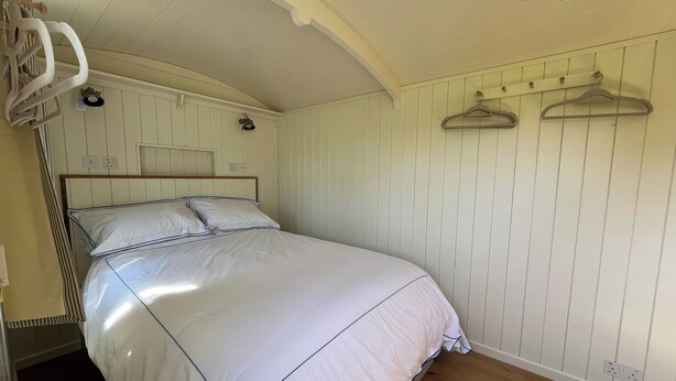 A neatly made bed in a room with wooden flooring, a white wall with a wooden headboard, and a ceiling with a curved design. - The Orchard (Dorchester)