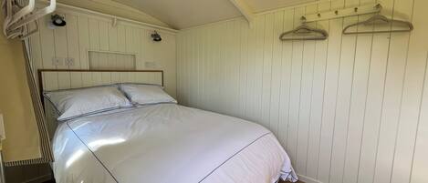 Un lit bien fait dans une pièce au plancher en bois, avec un mur blanc orné d’une tête de lit en bois et un plafond au décor incurvé.