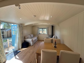 Una habitación acogedora con piso de madera, un sofá, una mesa de comedor con sillas y una ventana con cortinas.