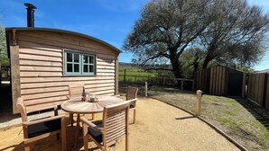 A wooden cabin with a round table and chairs, a window, and a chimney.