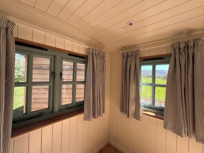 Una habitación con paneles de madera, dos ventanas con cortinas y un ventilador de techo.