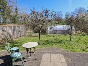 A patio with a table and chairs, a greenhouse, and a fenced area with trees. - Ystwyth Cottage (Newtown)