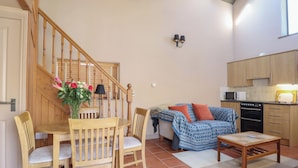 Uma sala de estar aconchegante com escada de madeira, mesa de jantar com cadeiras, sofá, mesa de centro e área de cozinha com eletrodomésticos.