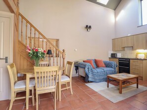 Ein gemütlicher Wohnbereich mit einer Holztreppe, einem Esstisch mit Stühlen, einer Couch, einem Couchtisch und einer Küchenzeile mit Geräten.