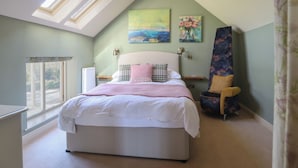 Quarto com cama, claraboias, janela, cadeira e obras de arte nas paredes.