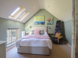 Ein Schlafzimmer mit Bett, Oberlichtern, einem Fenster, einem Sessel und Kunstwerken an den Wänden.