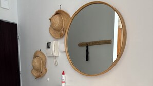 En vit byrå med lådor, en rund spegel med en träram och två halmhattar som hänger på väggen.