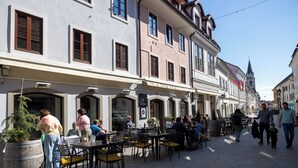 A street with outdoor seating, buildings with arched windows, and a flag. - Old Town Guest Accommodation (Kranj)