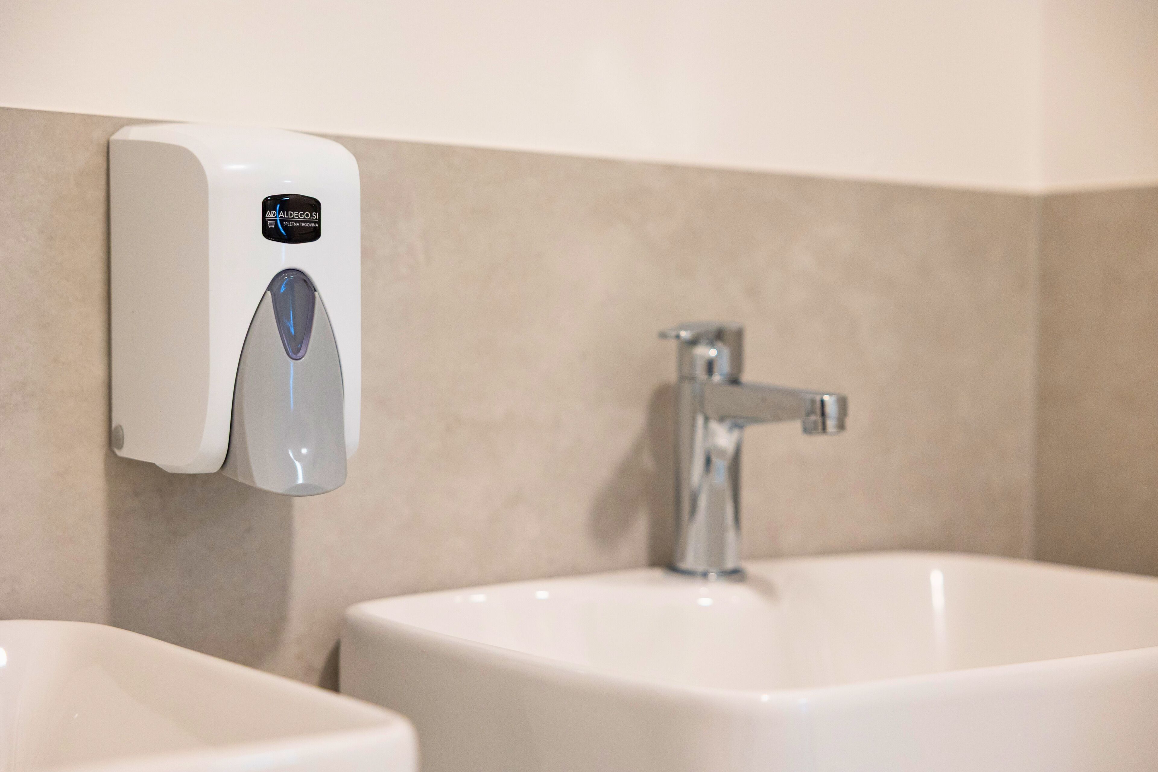 A bathroom with a hand sanitizer dispenser, a sink, and a faucet.