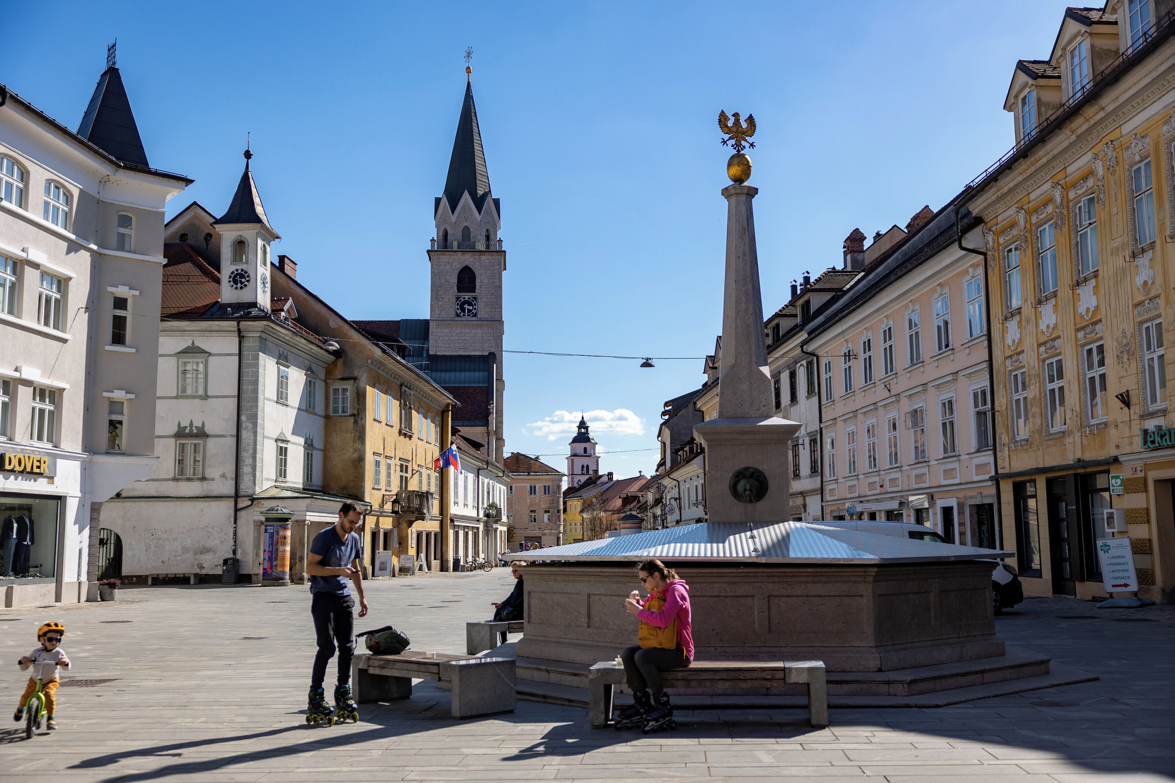 A public square with historic buildings, a clock tower, and a monument.