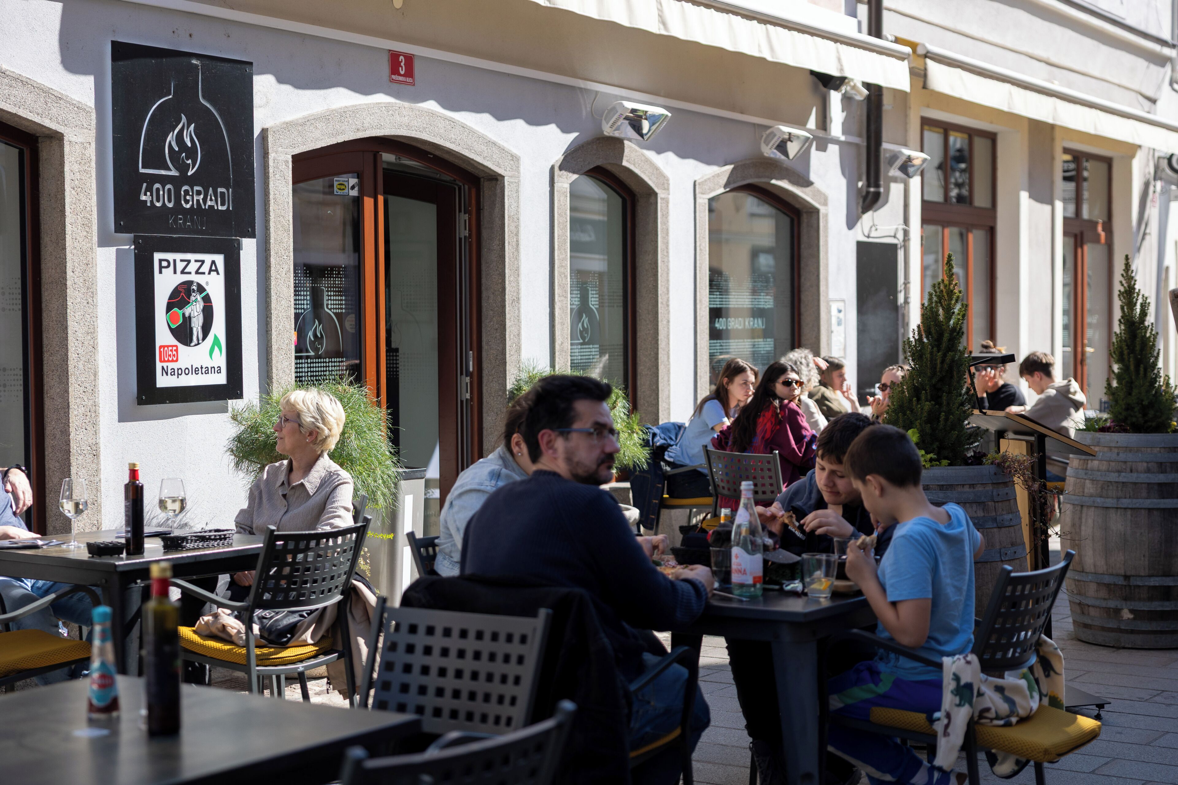 Ein Straßencafé mit Tischen und Stühlen, ein Schild für ein Pizza-Restaurant und ein Gebäude mit rundbogigen Fenstern.