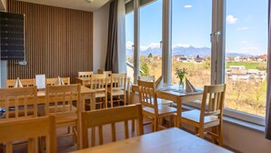 A dining area with wooden tables and chairs, large windows with a mountain view, and a vertical wooden panel on the wall. - Old Town Guest Accommodation (Kranj)