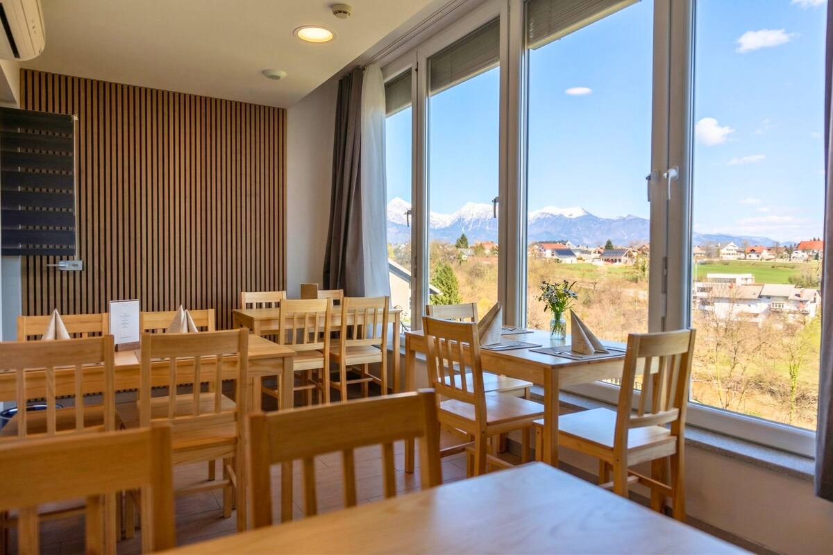 Ein Essbereich mit Holztischen und -stühlen, großen Fenstern mit Bergblick und einer vertikalen Holzverkleidung an der Wand.