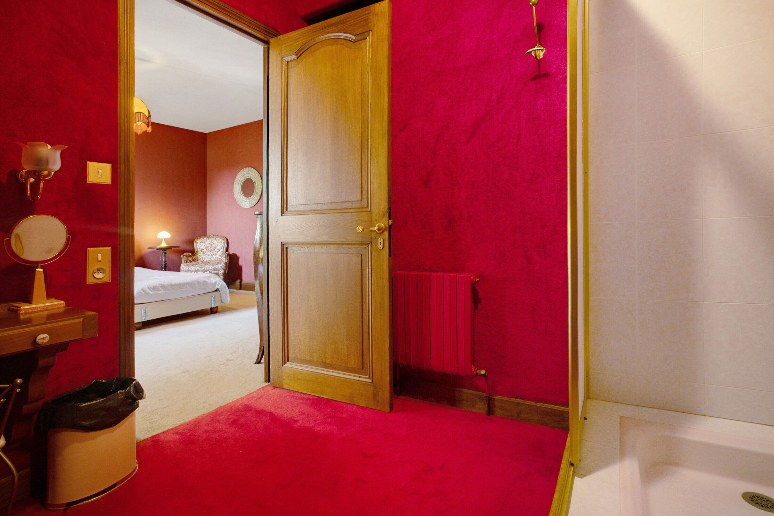 Una habitación con alfombra roja, puerta de madera, un radiador y una cama al fondo.