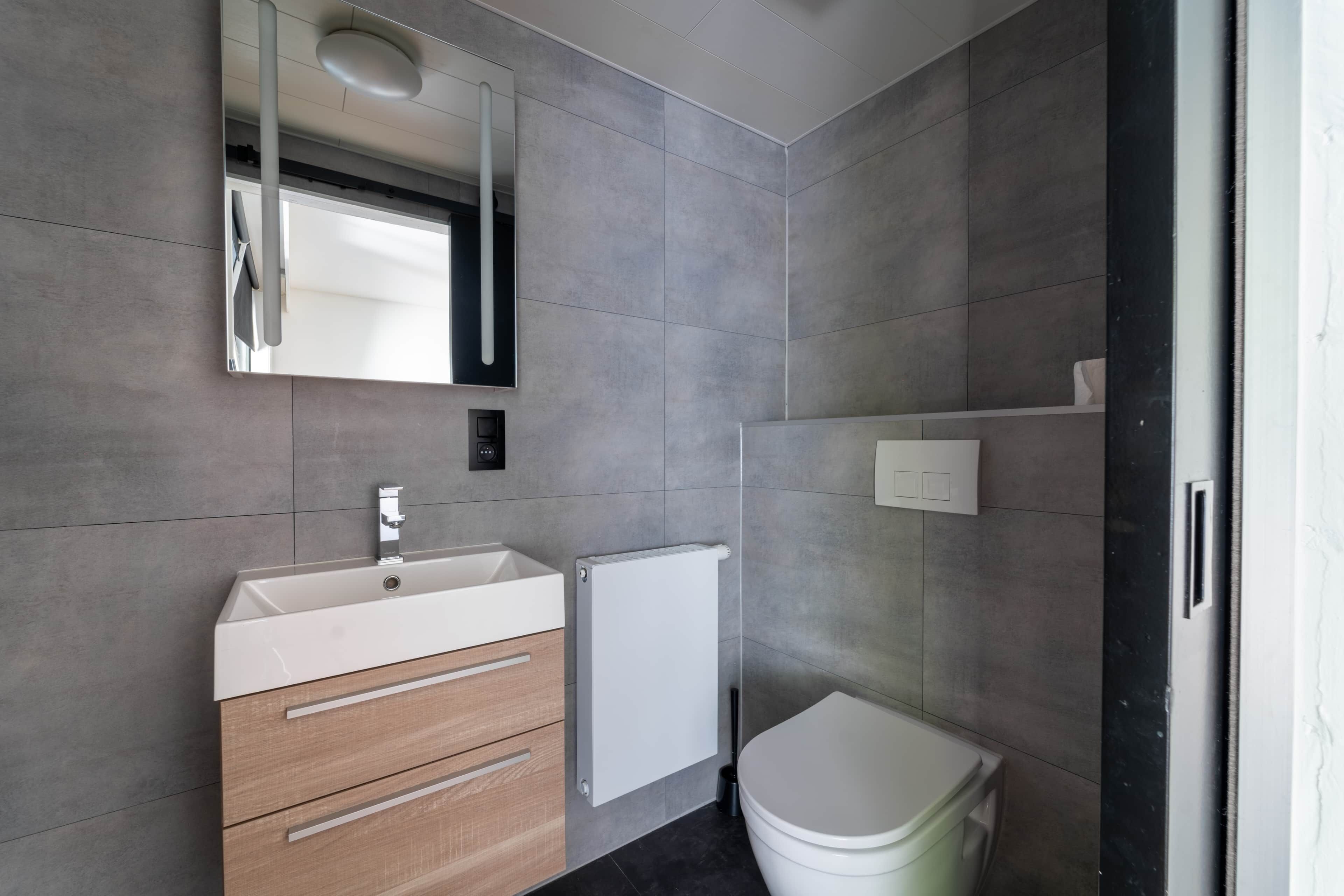 Un baño moderno con lavamanos blanco, mueble de madera y un inodoro.