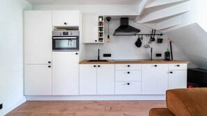 A modern kitchen with white cabinetry, a built-in oven, a black range hood, and hanging utensils. - Acacia 102 (Houthalen-Helchteren)