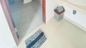 A bathroom with a toilet, shower, sink, and a small trash bin. - Cozzy Aesthetic Guest House (Ubud)