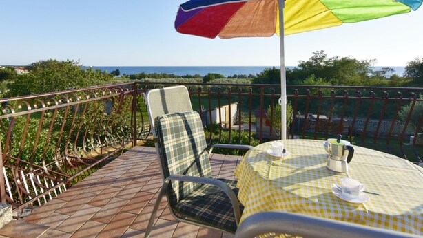 Un balcon avec une table à carreaux, une chaise en métal et un parasol coloré.