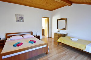 Ein Schlafzimmer mit einem hölzernen Bett, einem Nachttisch, einem Schminktisch und einem Spiegel, sowie einer Tür zu einem anderen Raum.