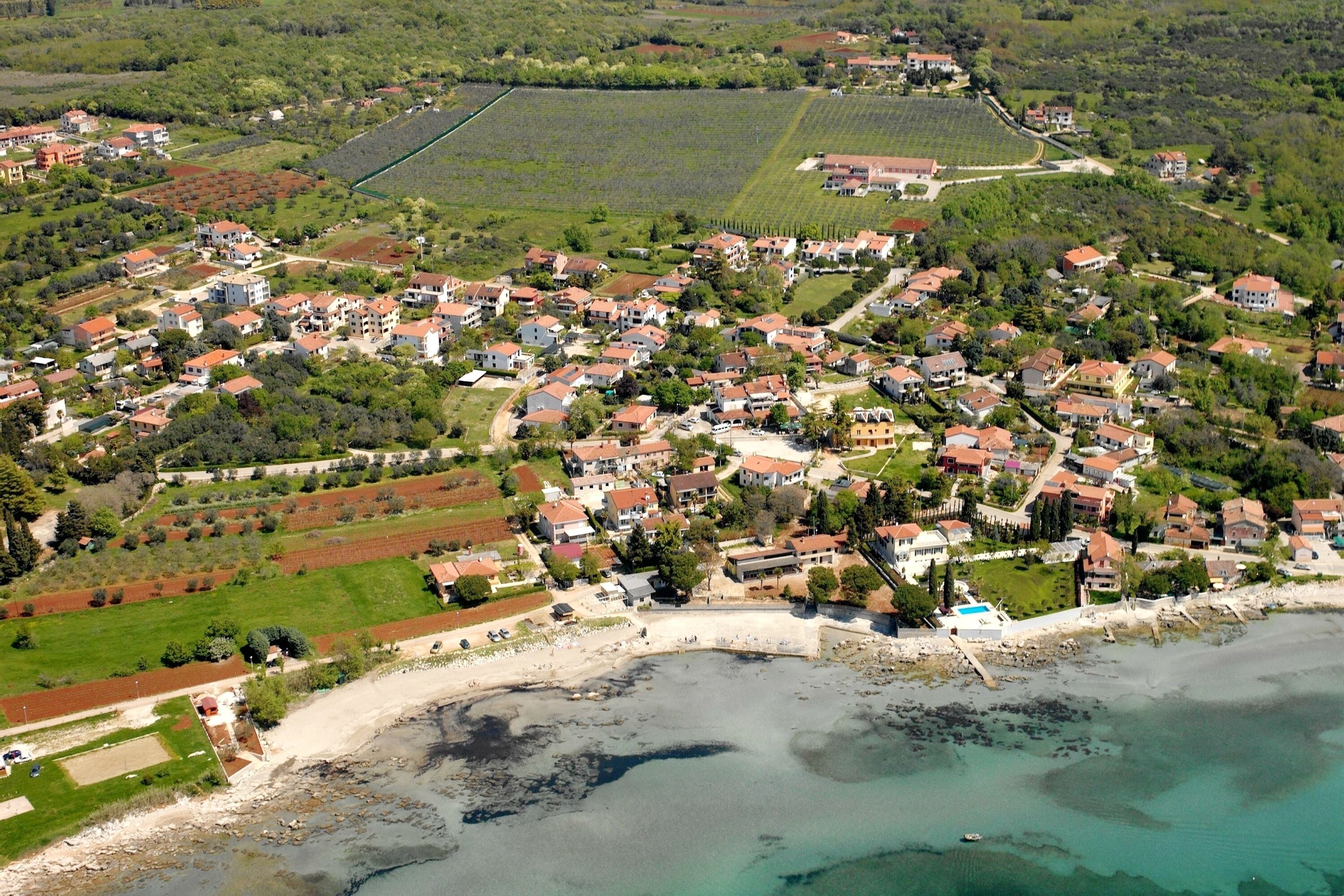 An aerial view of a coastal town with residential buildings, a beach, and agricultural fields.