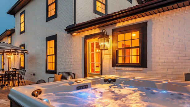 Ein Whirlpool mit einer Holzterrasse, einer Ziegelwand und einem Fenster mit warmem Licht.