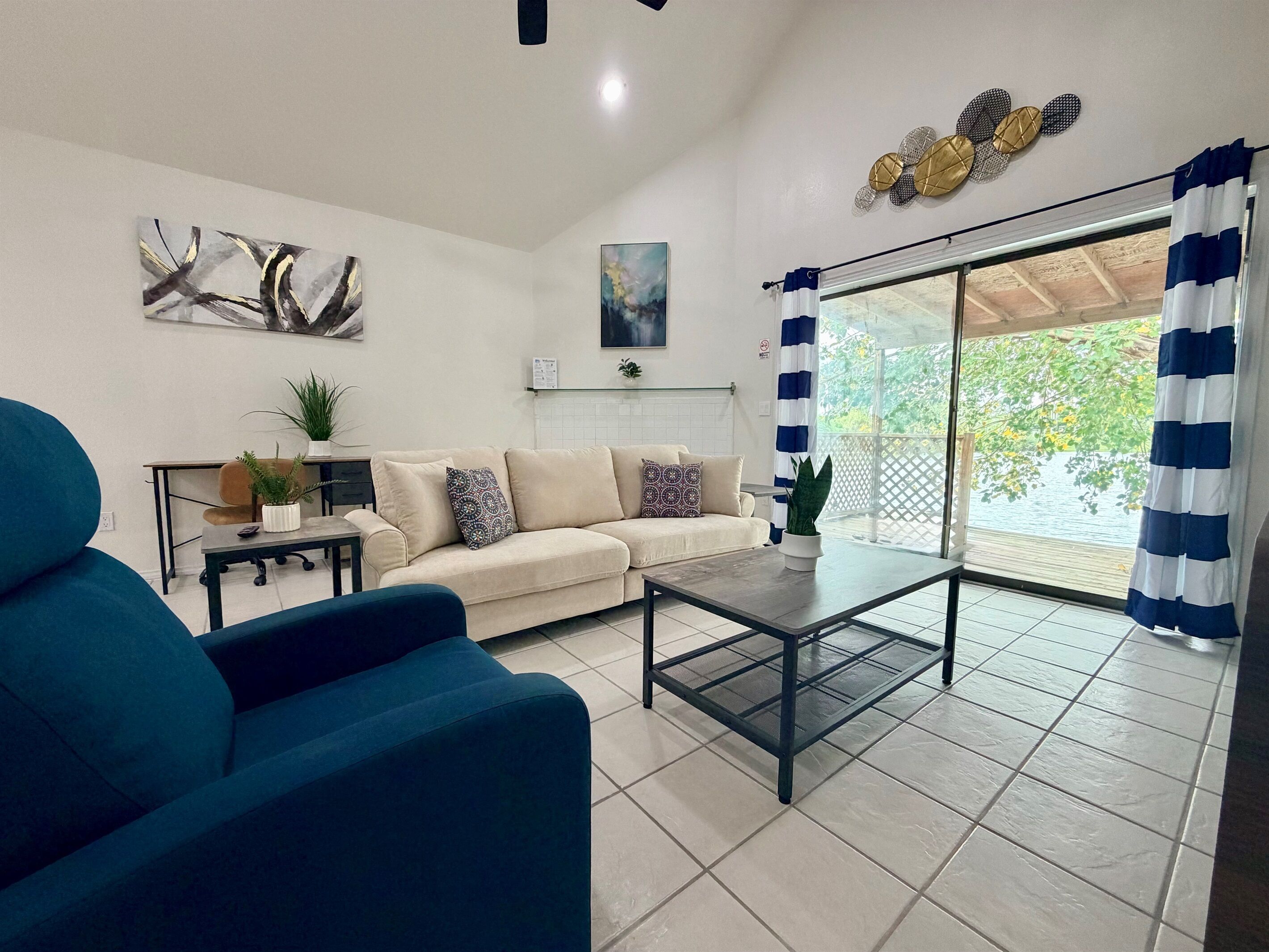 A living room with a sofa, a coffee table, a blue armchair, and a view through a glass door.