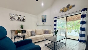A living room with a sofa, a coffee table, a blue armchair, and a view through a glass door. - Waterside at VICC - Cozy, Blissful Views! (Brownsville)