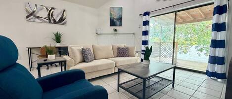 A living room with a sofa, a coffee table, a blue armchair, and a view through a glass door.