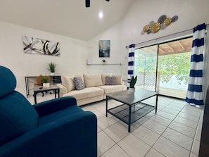A living room with a sofa, a coffee table, a blue armchair, and a view through a glass door. - Waterside at VICC - Cozy, Blissful Views! (Brownsville)