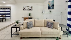 A living room with a beige sofa, a dining table, and chairs. There is a fireplace, a painting, and a plant on the wall. - Waterside at VICC - Cozy, Blissful Views! (Brownsville)
