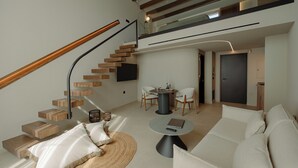 Un espacio habitable moderno con una escalera de madera, un comedor con sillas, un sofá y una mesa de centro redonda.