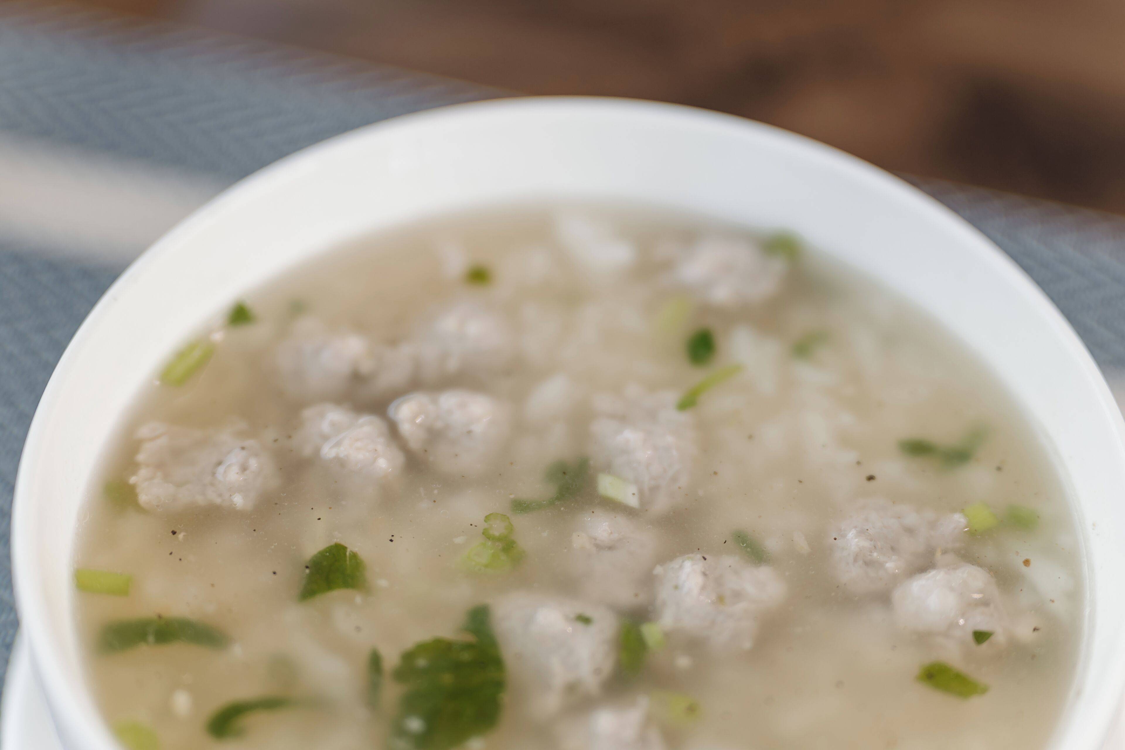 A bowl of soup with meatballs and green herbs.