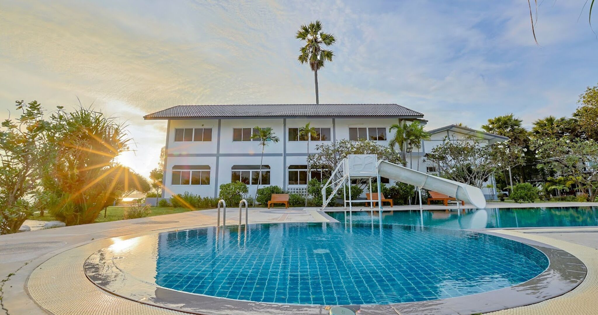 A swimming pool with a slide, a building with multiple windows, and palm trees.