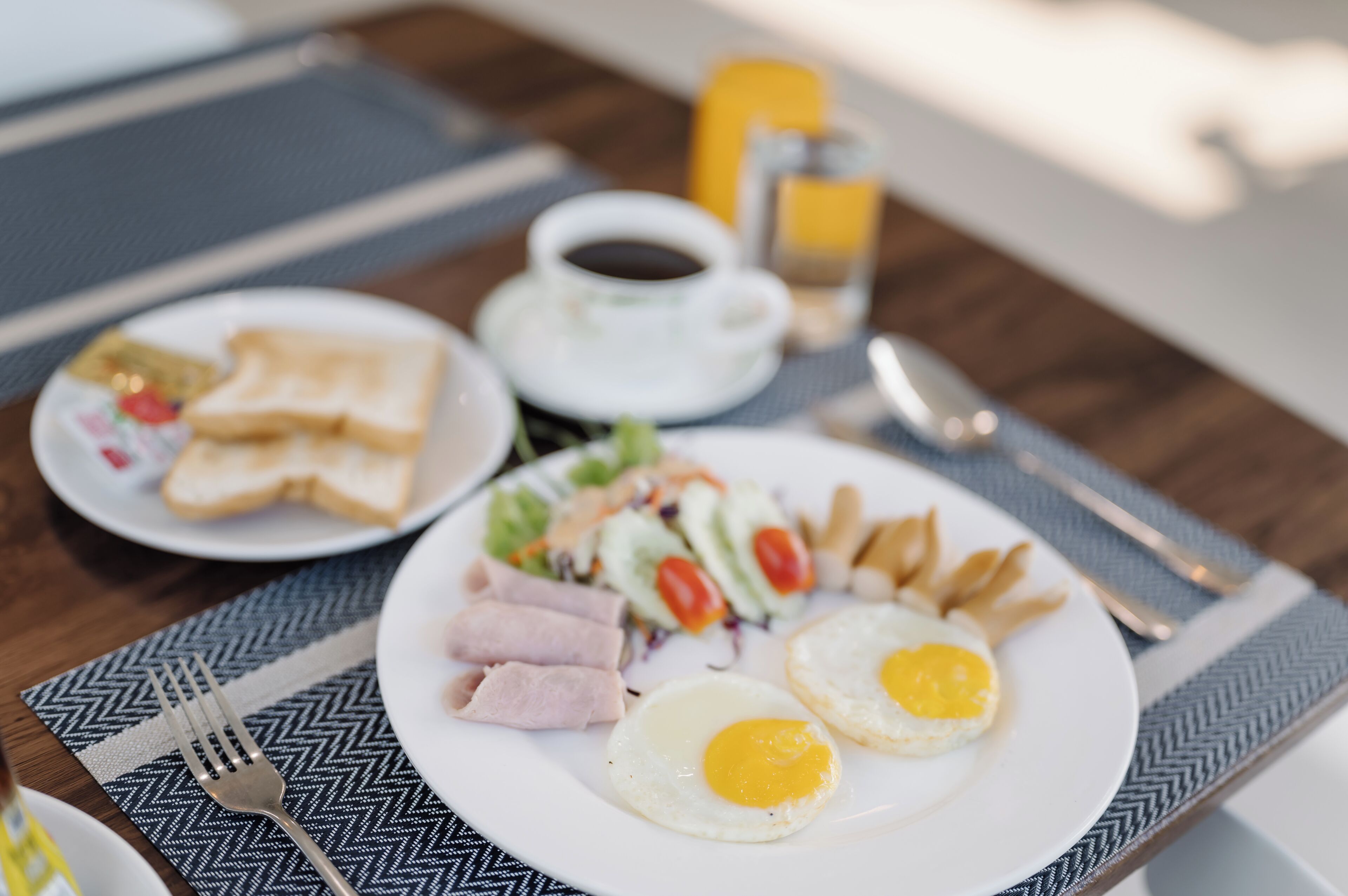 Un plato de desayuno con huevos, jamón y verduras, una taza de café y tostadas sobre una mesa.