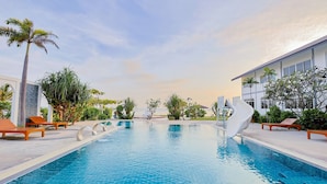 Una piscina con sillones de descanso, palmeras y un edificio de fachada blanca.