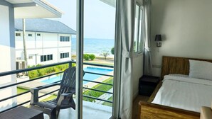 Habitación de hotel con balcón, una cama, una silla y vistas al océano y una piscina.