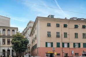 A multi-story building with a beige facade and green shutters, featuring a ground-floor shop with a visible sign. - Cute Nest near the Center by Wonderful Italy (Genoa)