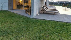 Una casa moderna con ingresso tramite una porta in vetro, un patio con poltrone relax e vista sul paesaggio.