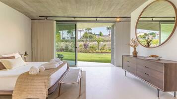 A bedroom with a bed, a bench, a dresser, a mirror, and a sliding glass door to a garden.