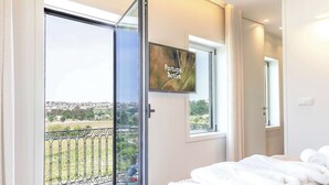 Una camera da letto con un letto, una TV, un balcone e vista panoramica, più una porta.