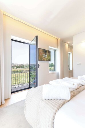 Un dormitorio con cama, televisión, balcón con vistas y una puerta.